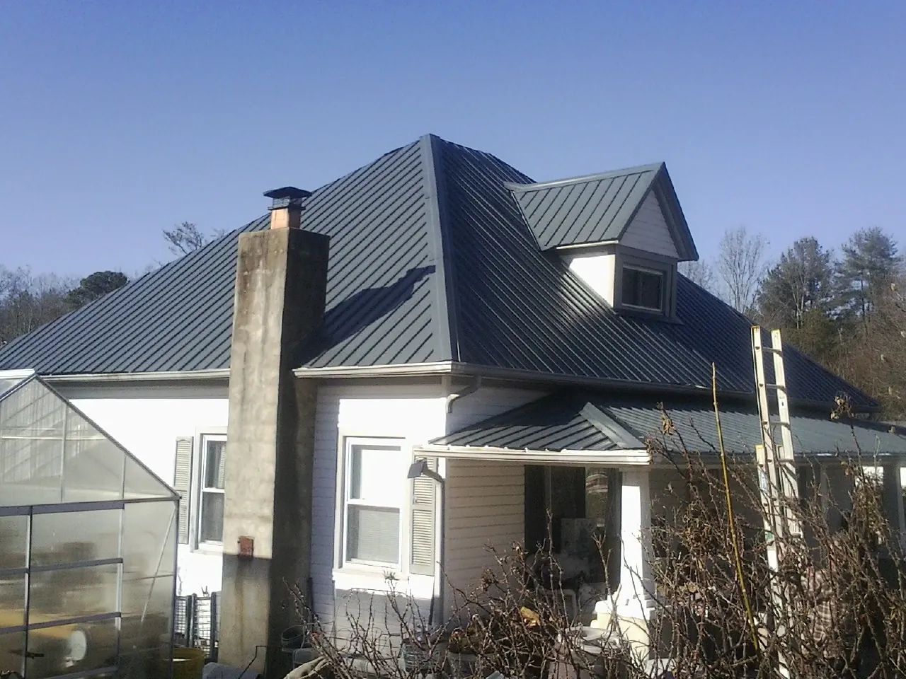 Dark blue standing seam metal roof on a white farmhouse with dormer — Slate & Tile Roof Repair by Roofing Brothers in Greenleaf
