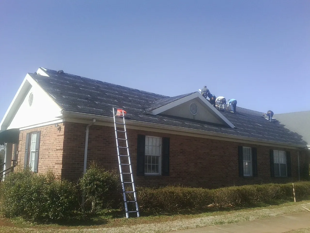 Crew tearing shingles off a brick ranch roof with a ladder set — Metal Roof Repair work by our crew in Greenleaf