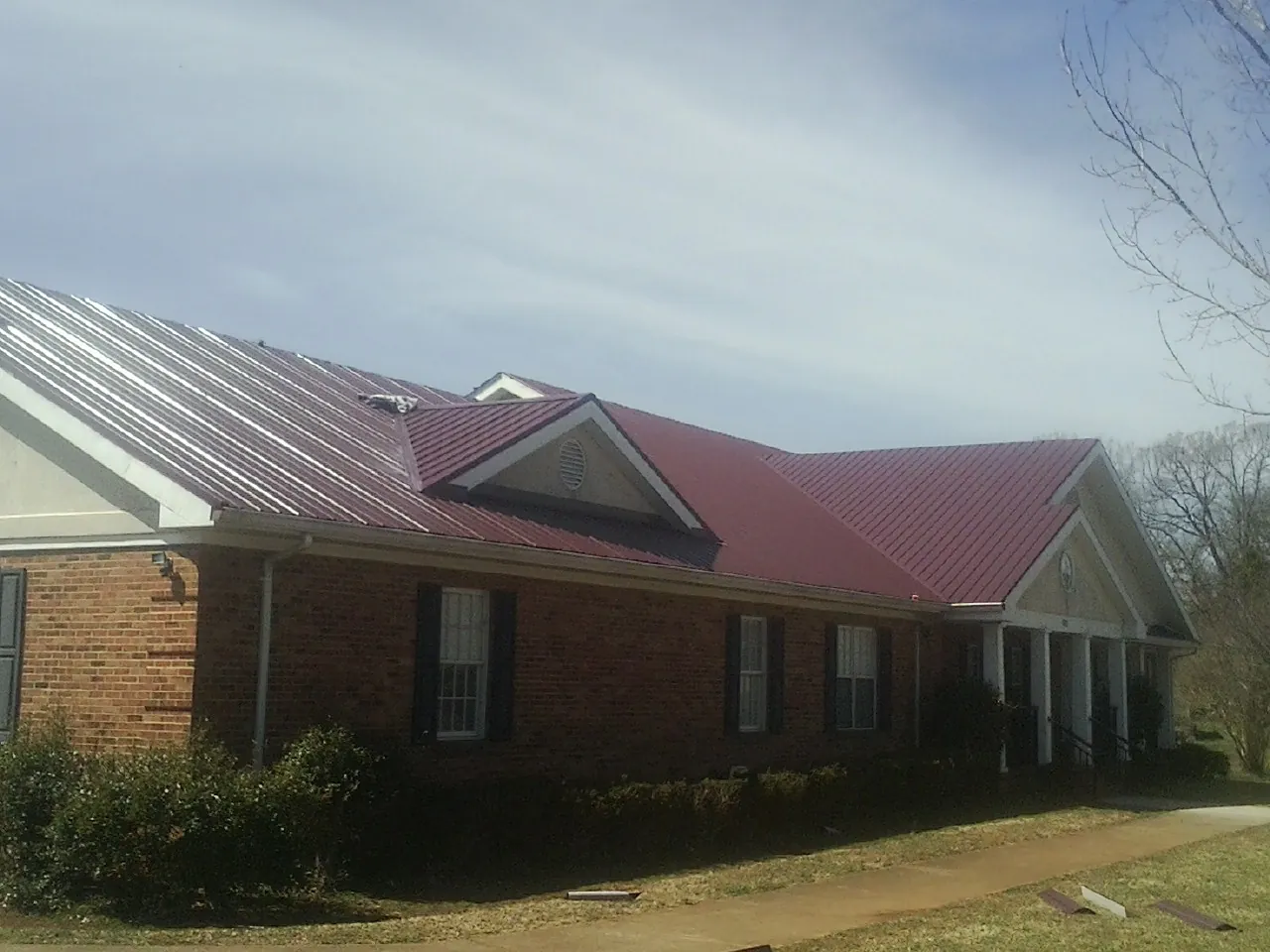 Red metal roof with gabled entries on a long brick building, from a Hail Damage Roof Repair job in Greenleaf
