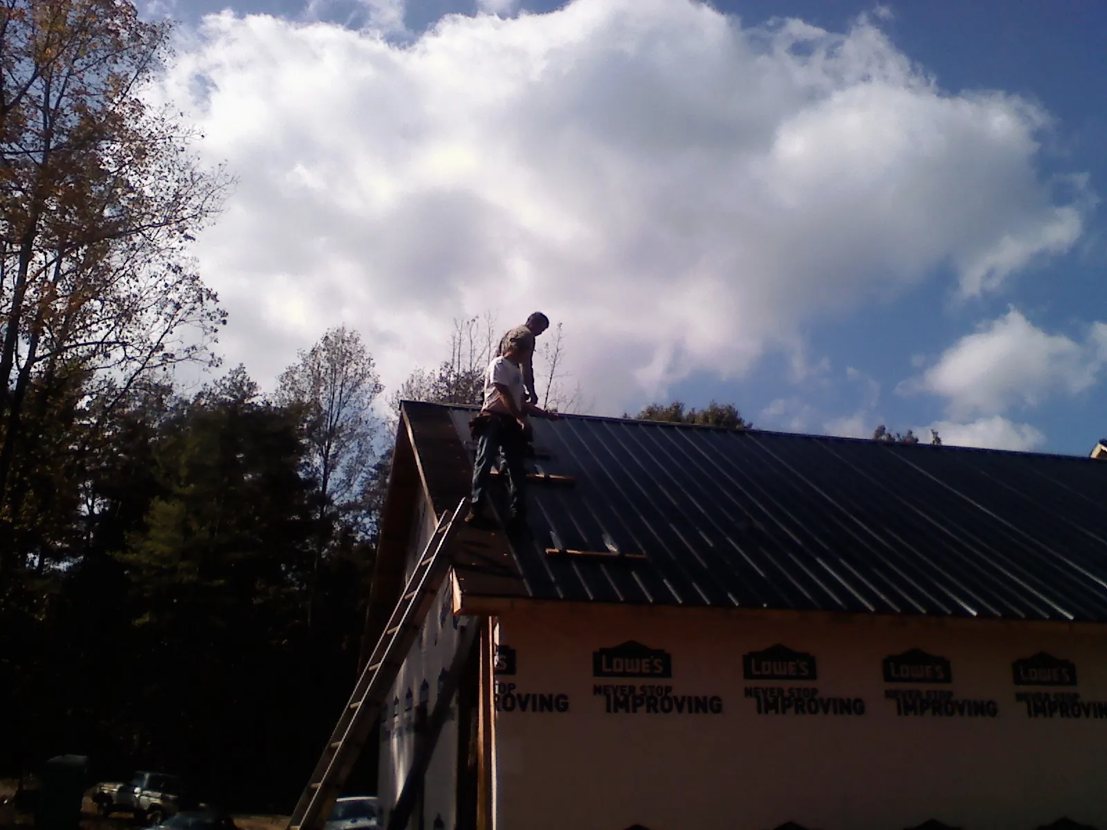 Roofer fastening dark metal panels high against a cloudy sky, from a Roof Inspection job in Greenleaf