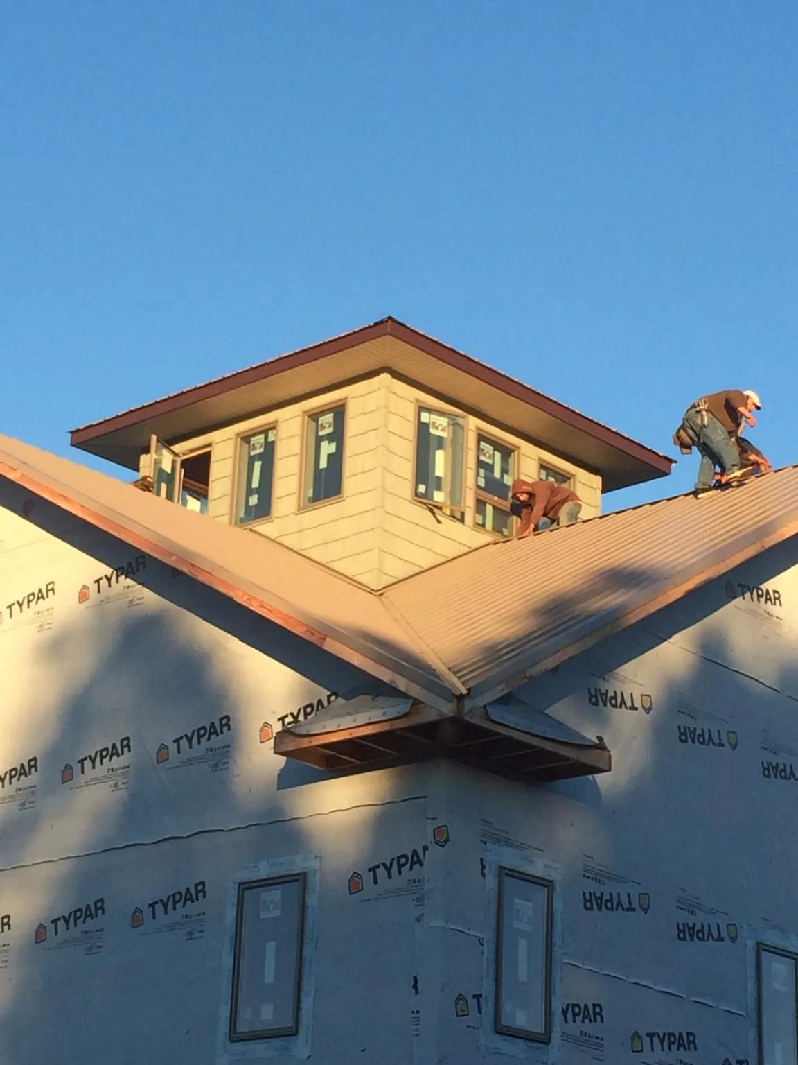 Roofers working around a rooftop cupola on a new metal roof at sunset in Greenleaf